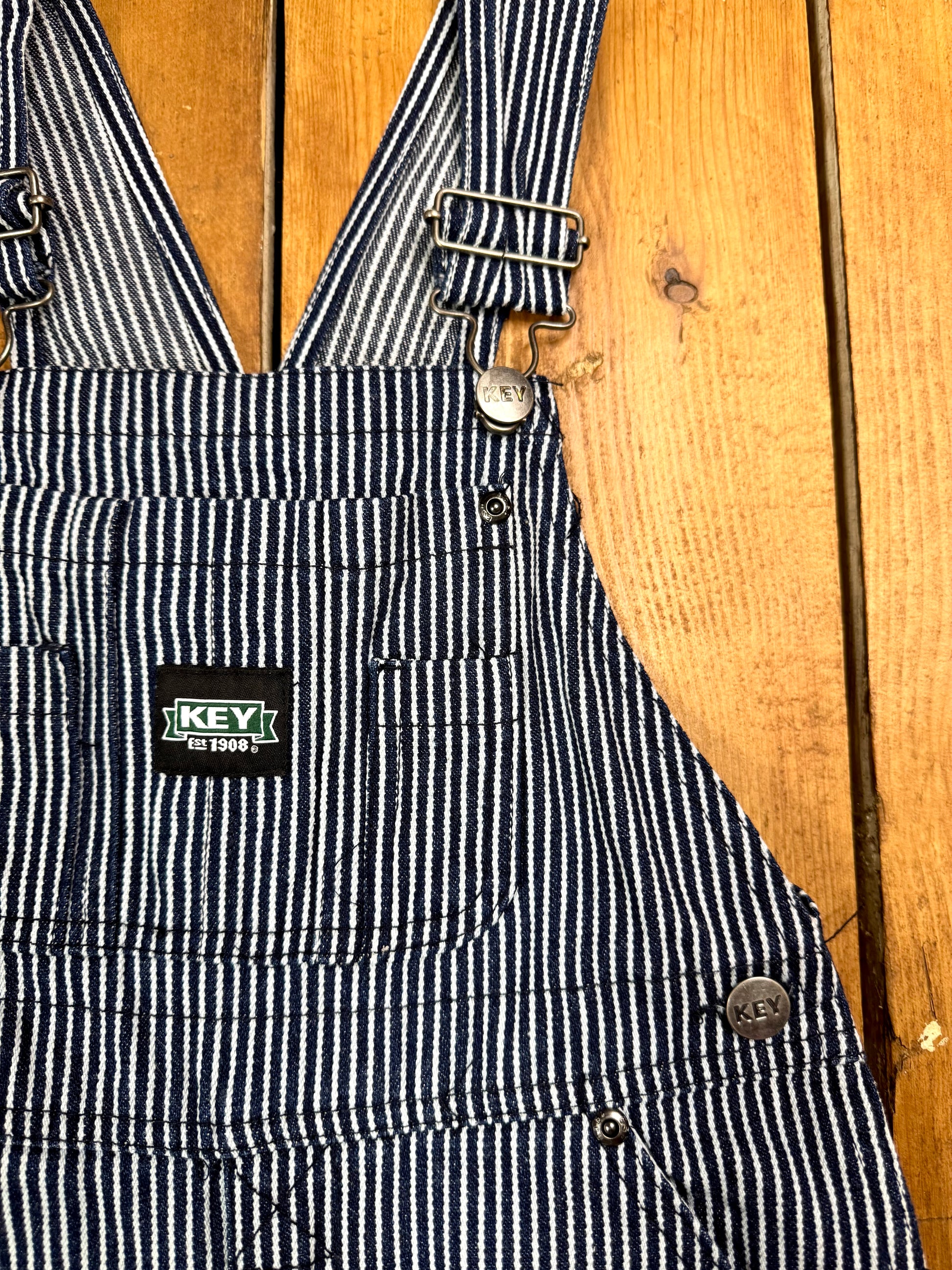 Vintage Key kids hickory stripe dungarees, adjustable straps, utility pockets, and authentic workwear styling. A timeless American heritage piece. Handpicked for Bee Tiny kids vintage.