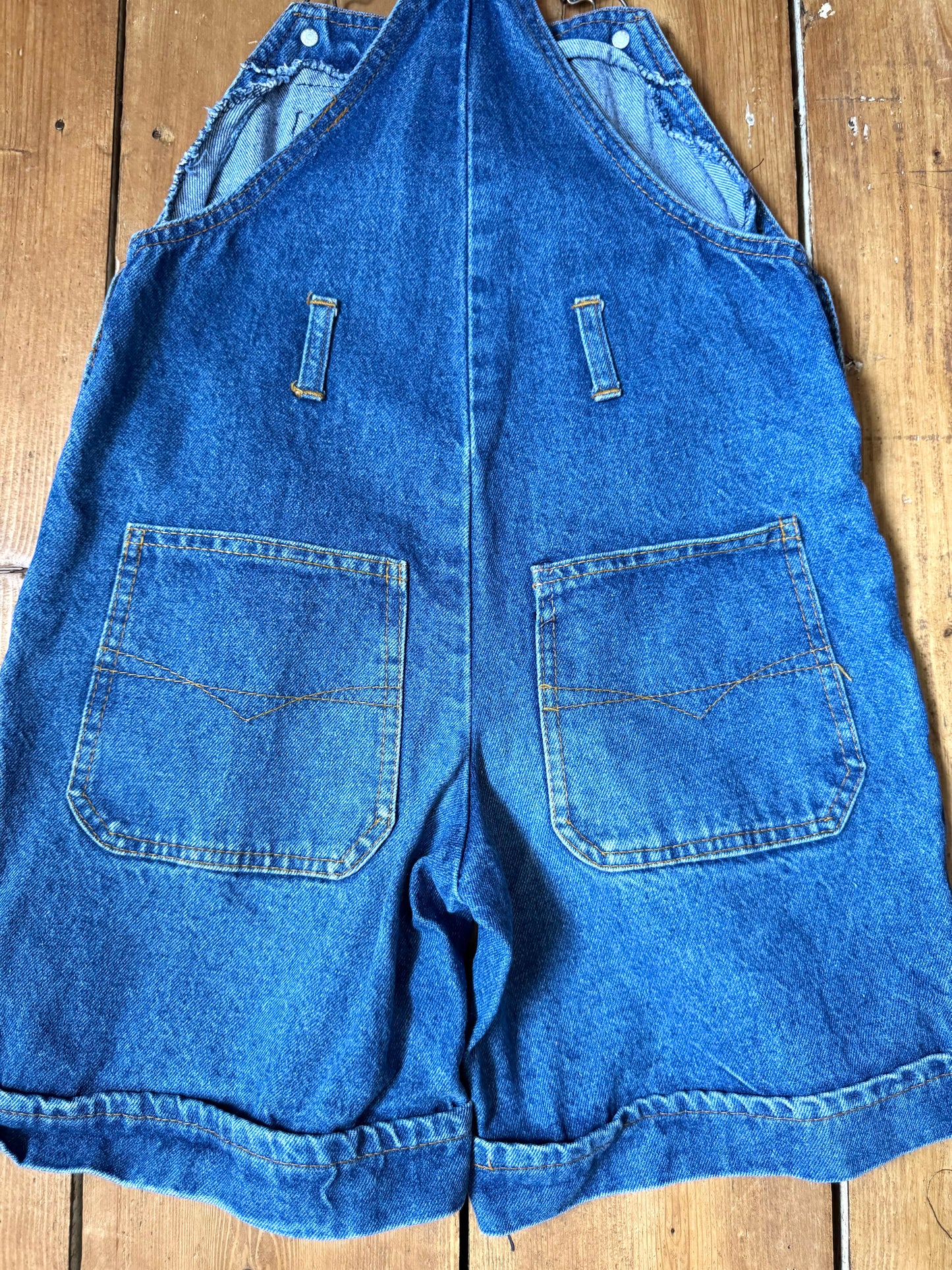 Vintage blue denim dungaree shorts for kids with embroidered chest detail and adjustable straps. Authentic late 80s/early 90s, handpicked for Bee Tiny kids vintage.