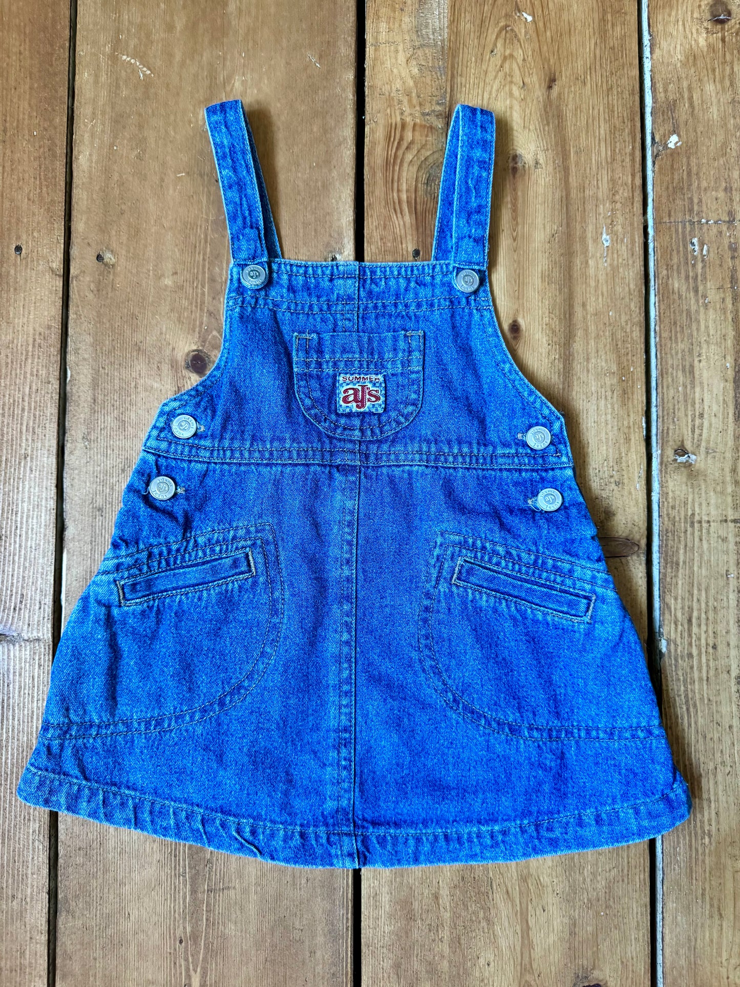 Vintage baby dress bundle featuring an Adams denim pinafore and pink gingham summer dress. Two timeless outfits for babies aged 6–9 months. Handpicked for Bee Tiny kids vintage.