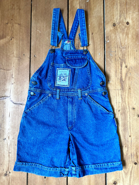 Vintage blue denim dungaree shorts for kids with embroidered chest detail and adjustable straps. Authentic late 80s/early 90s, handpicked for Bee Tiny kids vintage.