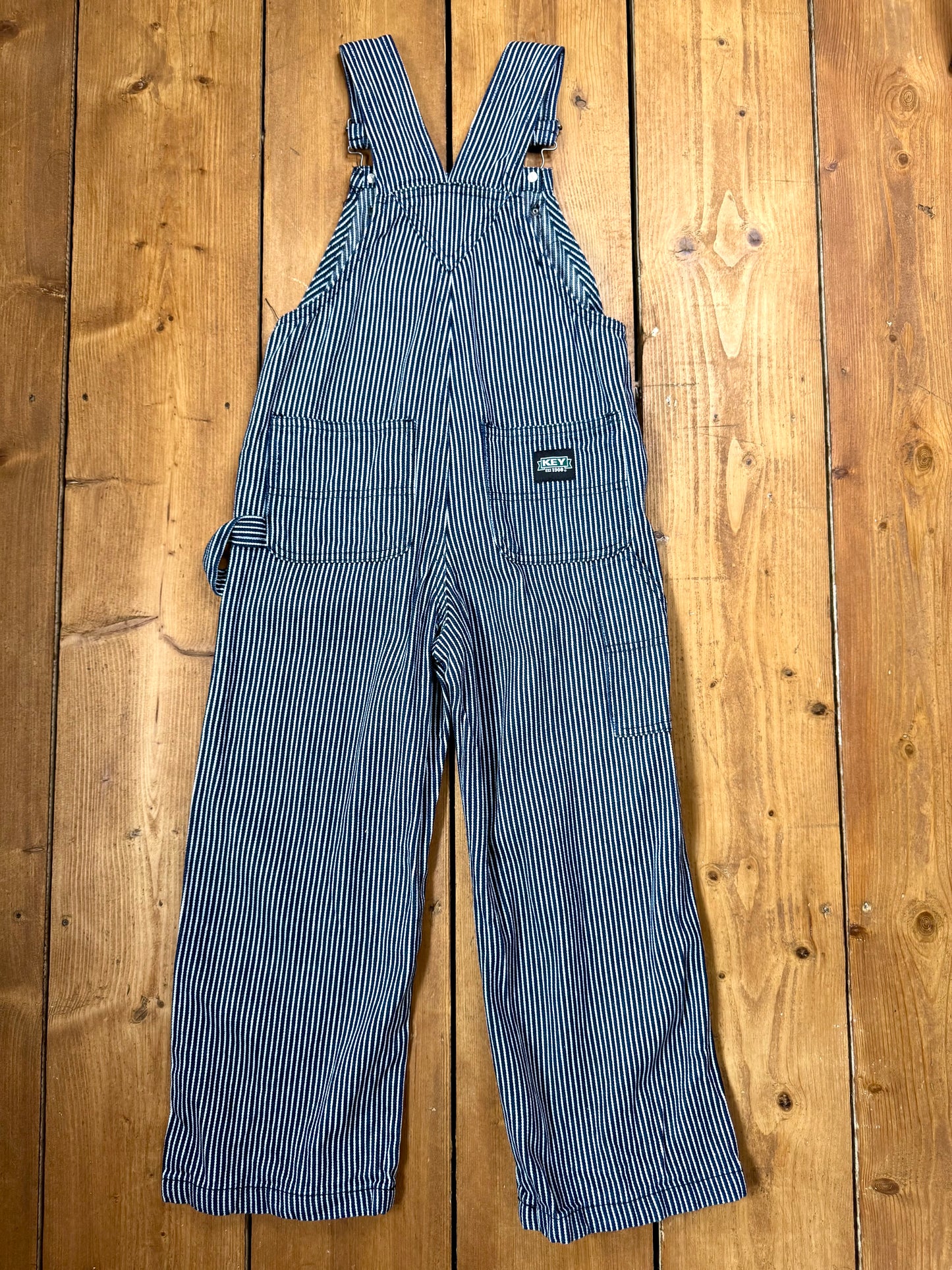 Vintage Key kids hickory stripe dungarees, adjustable straps, utility pockets, and authentic workwear styling. A timeless American heritage piece. Handpicked for Bee Tiny kids vintage.