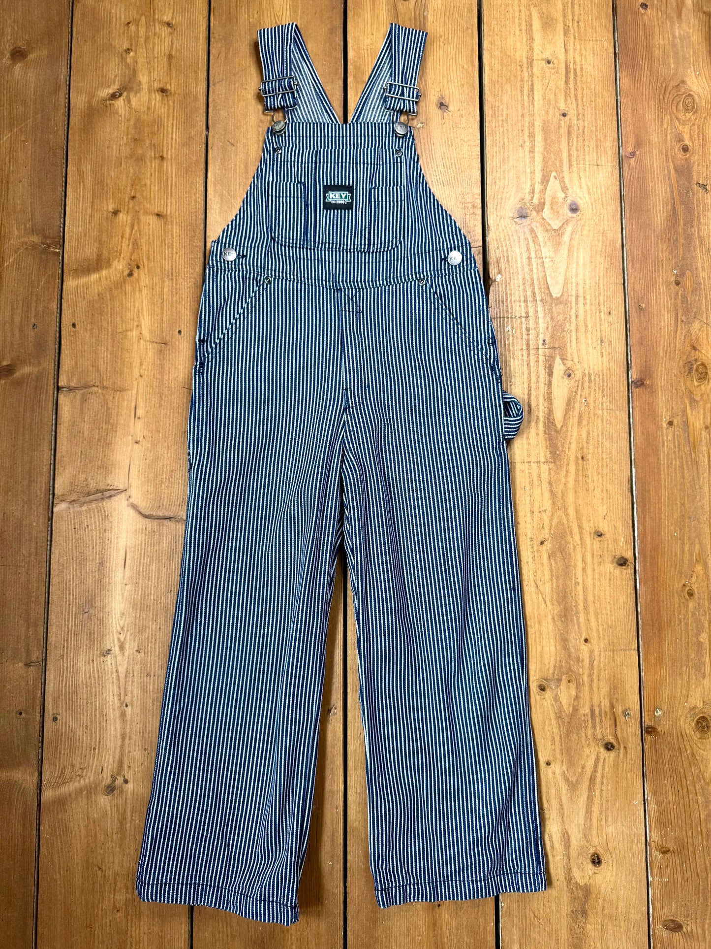 Vintage Key kids hickory stripe dungarees, adjustable straps, utility pockets, and authentic workwear styling. A timeless American heritage piece. Handpicked for Bee Tiny kids vintage.