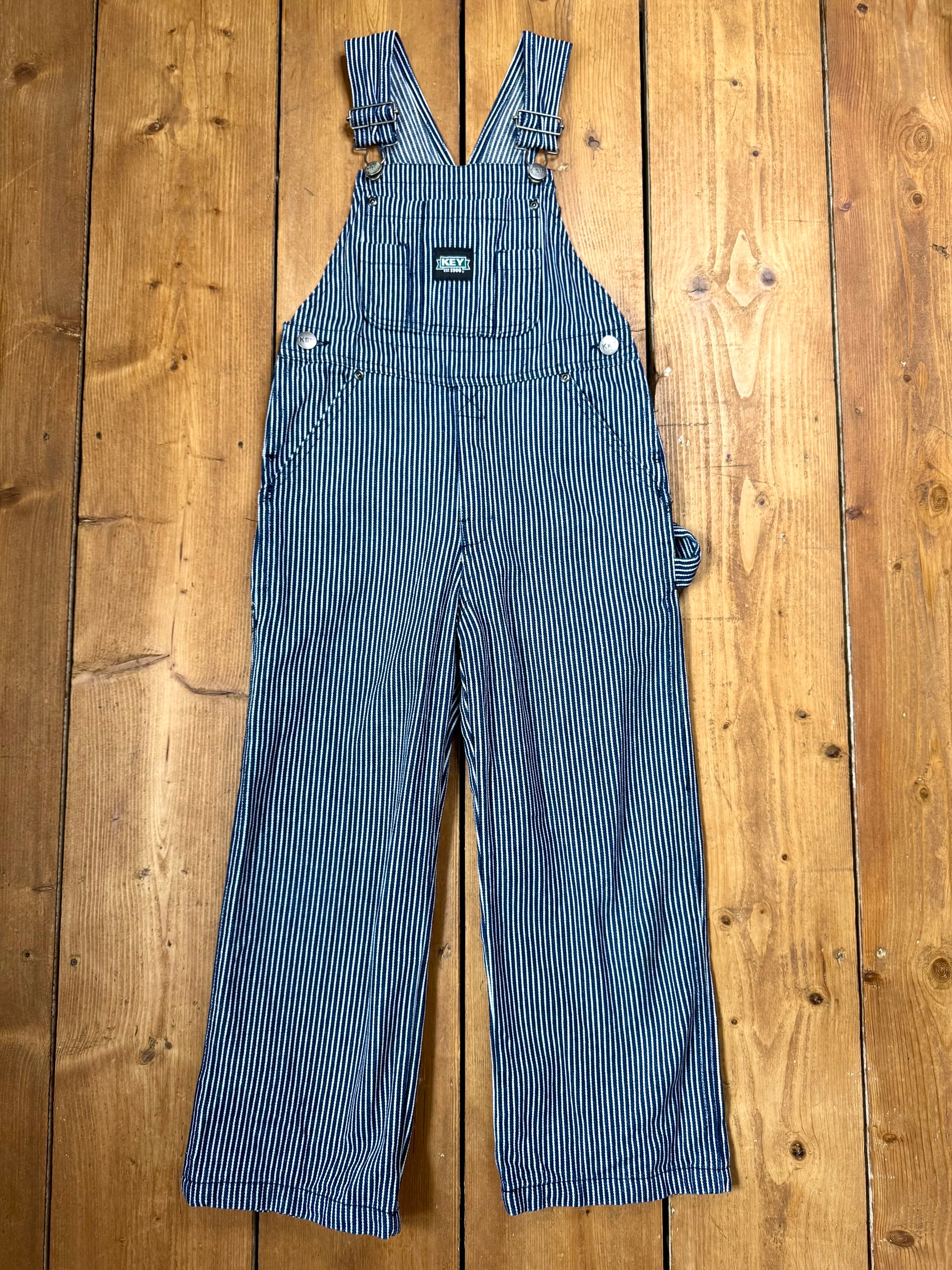 Vintage Key kids hickory stripe dungarees, adjustable straps, utility pockets, and authentic workwear styling. A timeless American heritage piece. Handpicked for Bee Tiny kids vintage.
