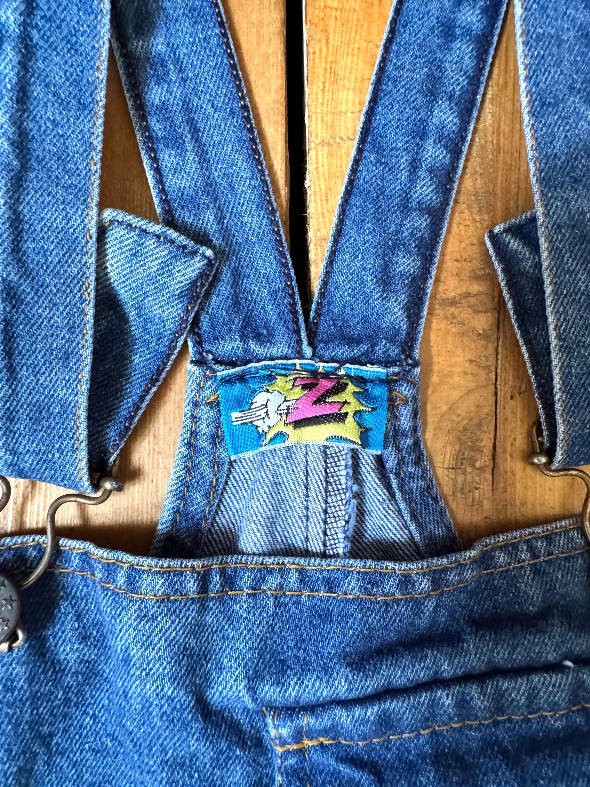 Vintage blue denim dungaree shorts for kids with embroidered chest detail and adjustable straps. Authentic late 80s/early 90s, handpicked for Bee Tiny kids vintage.