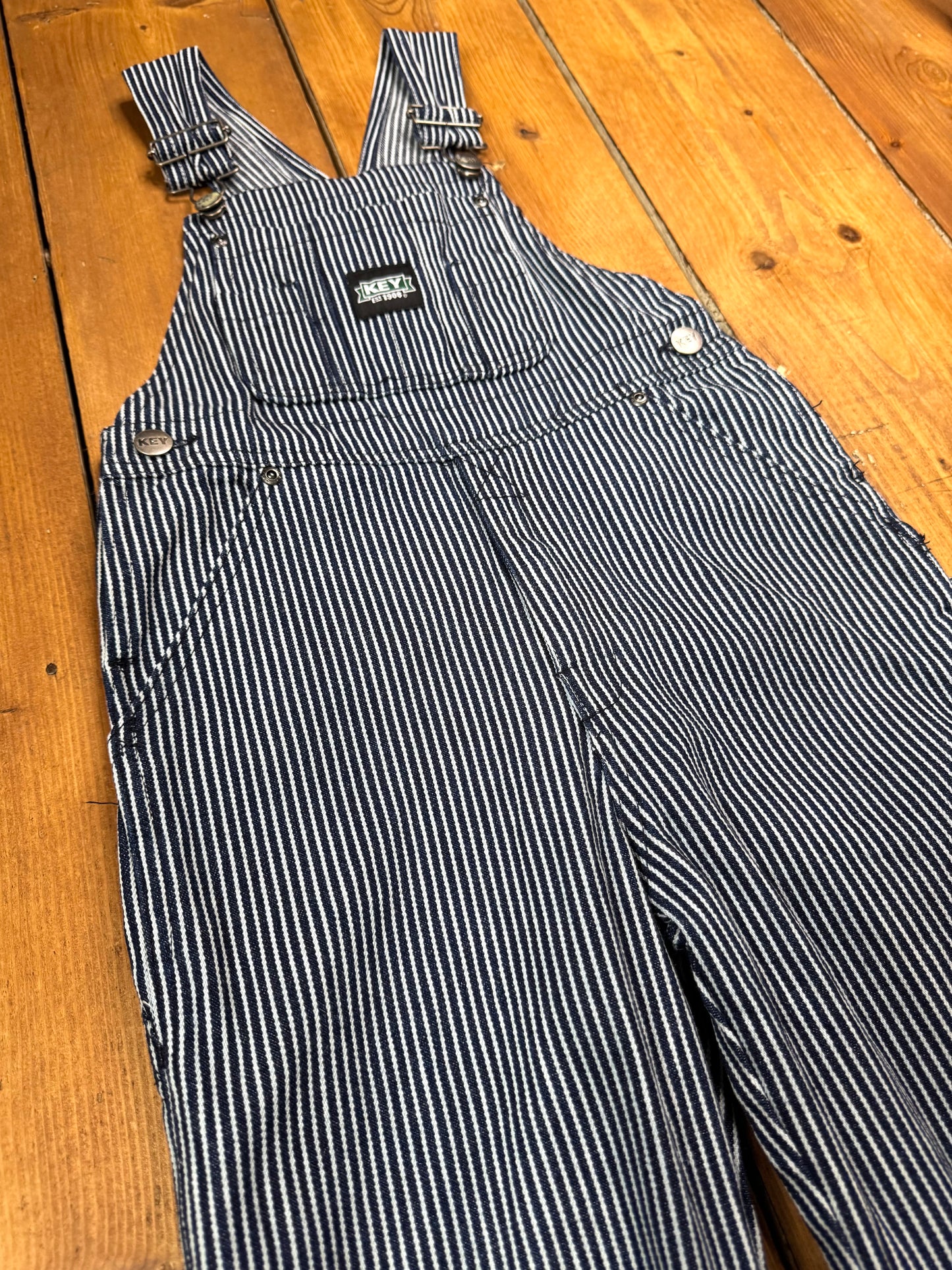 Vintage Key kids hickory stripe dungarees, adjustable straps, utility pockets, and authentic workwear styling. A timeless American heritage piece. Handpicked for Bee Tiny kids vintage.