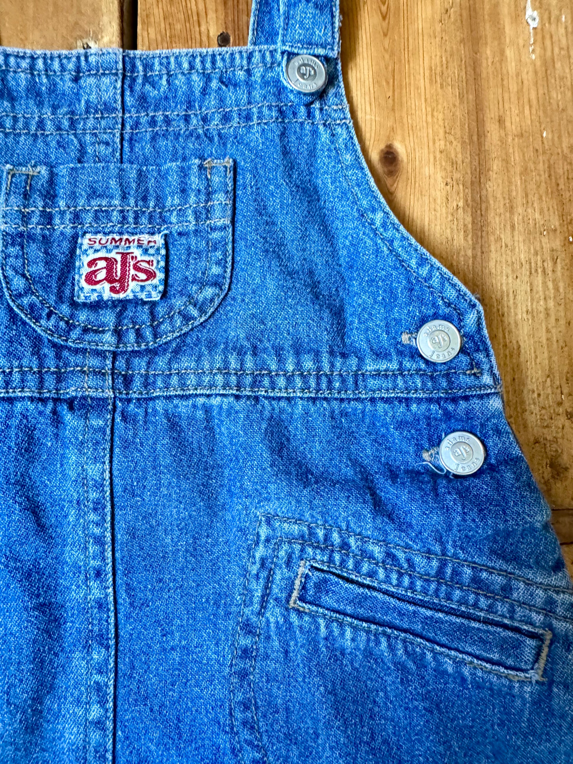 Vintage baby dress bundle featuring an Adams denim pinafore and pink gingham summer dress. Two timeless outfits for babies aged 6–9 months. Handpicked for Bee Tiny kids vintage.