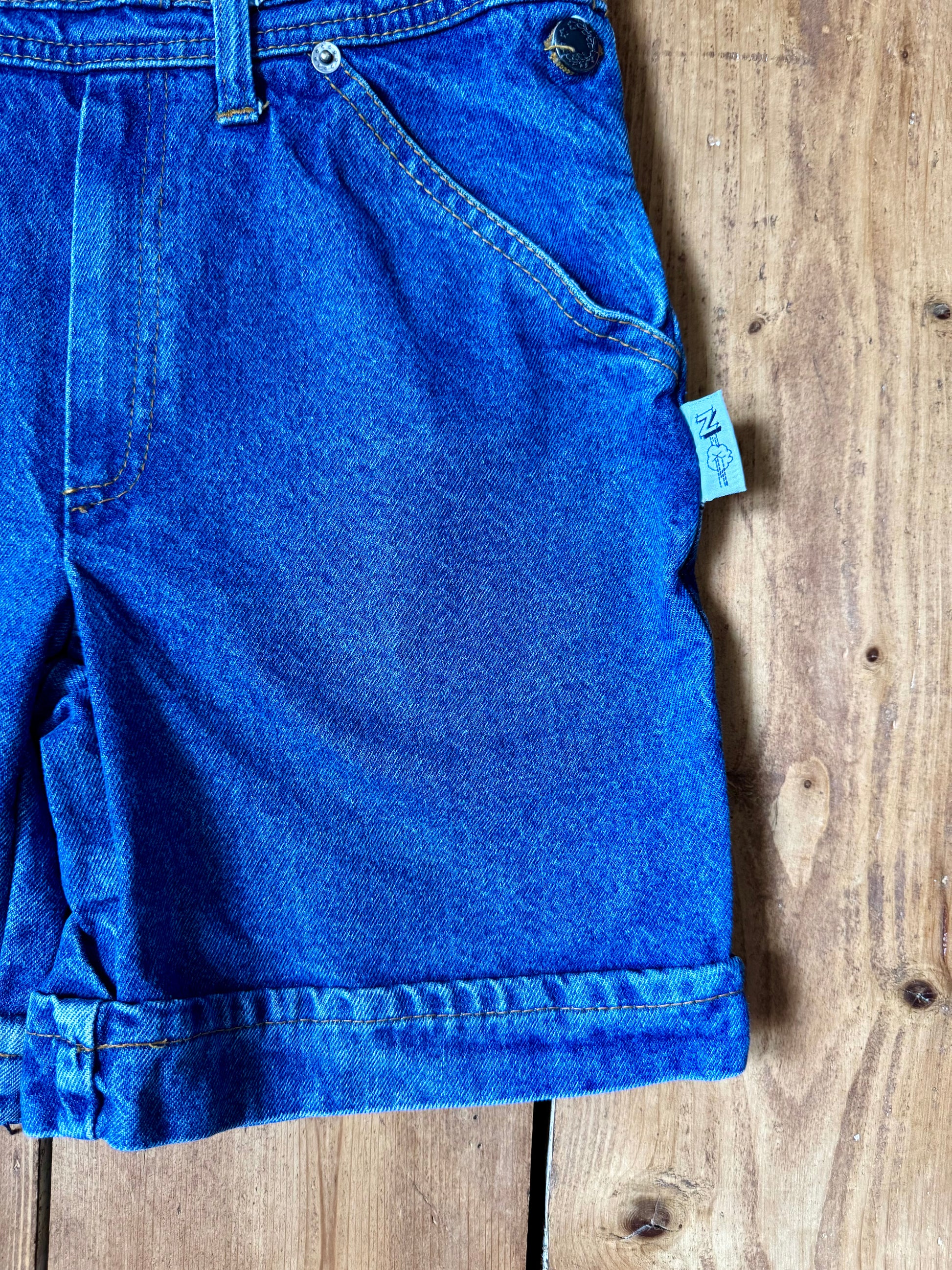 Vintage blue denim dungaree shorts for kids with embroidered chest detail and adjustable straps. Authentic late 80s/early 90s, handpicked for Bee Tiny kids vintage.