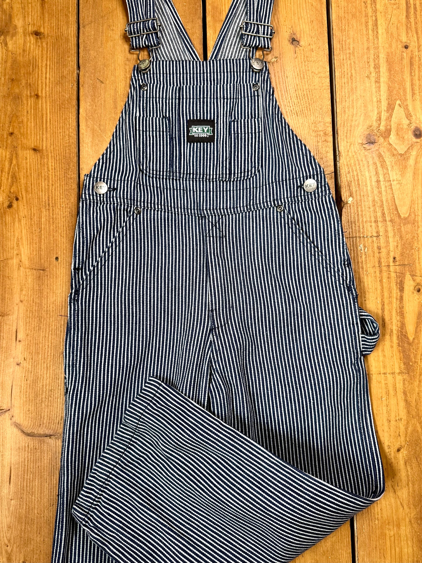 Vintage Key kids hickory stripe dungarees, adjustable straps, utility pockets, and authentic workwear styling. A timeless American heritage piece. Handpicked for Bee Tiny kids vintage.