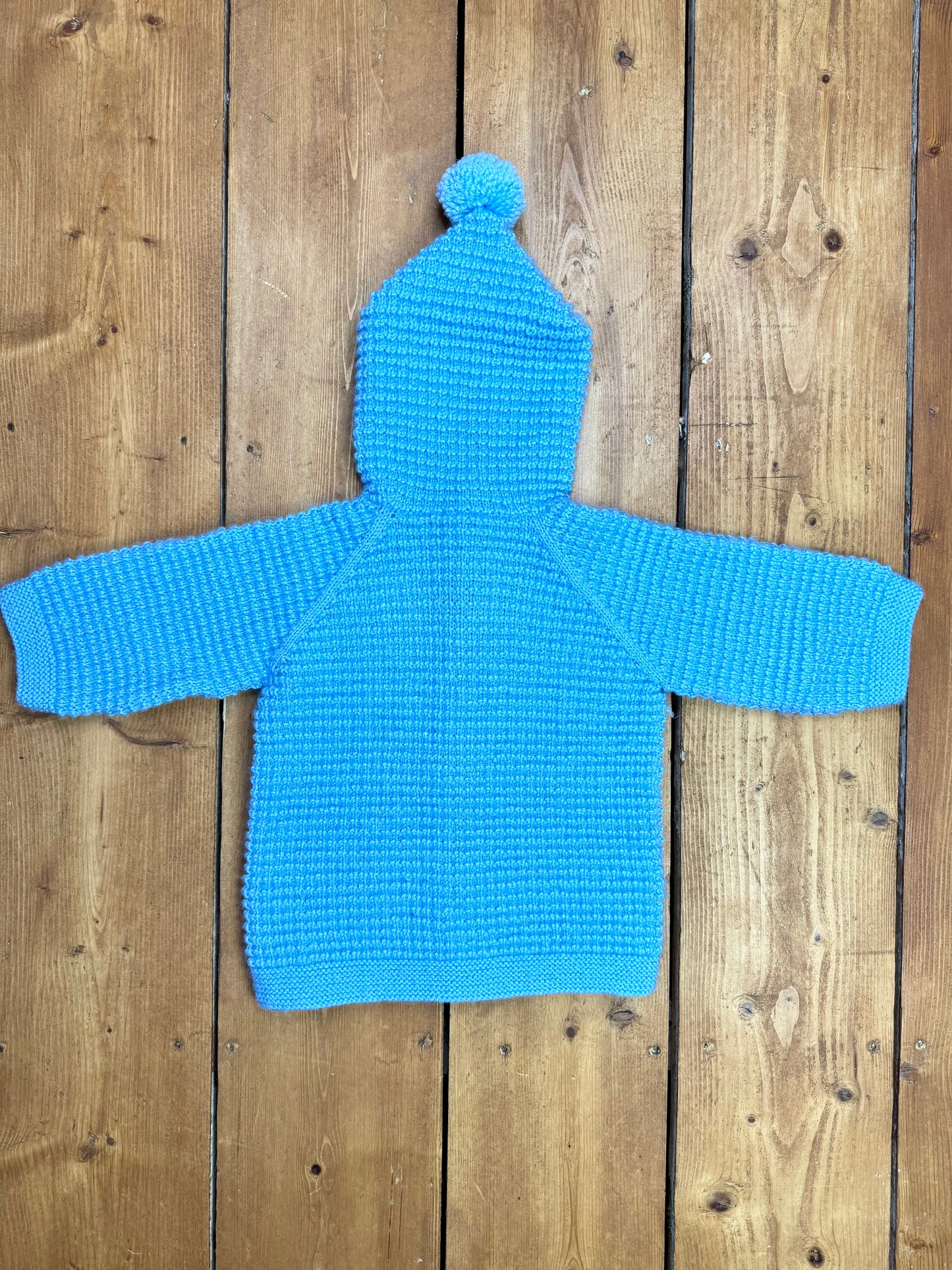 Blue knitted baby cardigan with pom pom hood